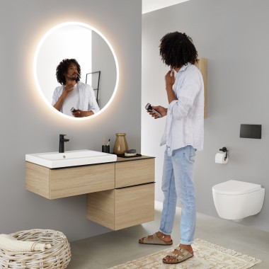 Homem a olhar para si próprio num espelho redondo Geberit Option iluminado Homem a olhar para si próprio num espelho redondo Geberit Option iluminado