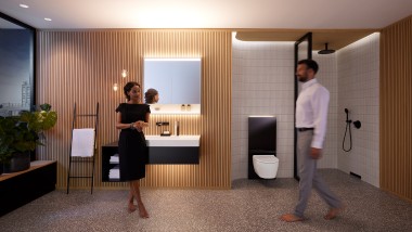 Homem e mulher numa casa de banho perfeitamente iluminada com móveis de casa de banho e sanitários Geberit ONE (© Geberit)