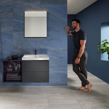 Homem encostado à parede numa casa de banho azul com lavatório Mix & Match da Geberit Homem encostado à parede numa casa de banho azul com lavatório Mix & Match da Geberit