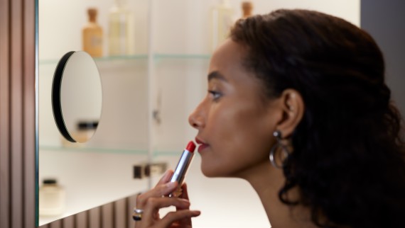Mulher a colocar lápis de lábios em frente a um espelho de aumento (© Geberit)