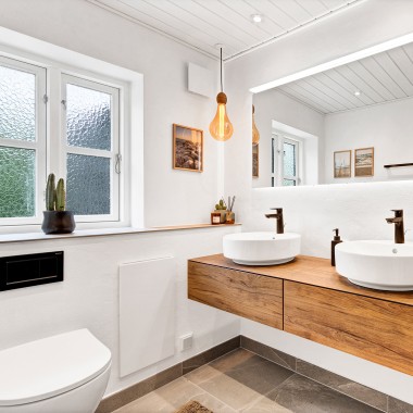 Casa de banho renovada e luminosa com dois lavatórios redondos, um espelho grande e móveis de casa de banho em madeira (© @triner2 e @strandparken3)