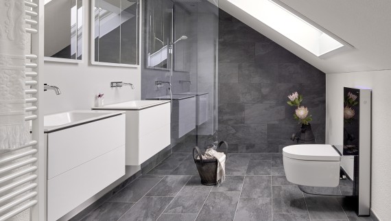 Casa de banho com cobertura inclinada e produtos da série de casas de banho Geberit ONE e Geberit AquaClean com Monolith Casa de banho com cobertura inclinada e produtos da série de casas de banho Geberit ONE e Geberit AquaClean com Monolith