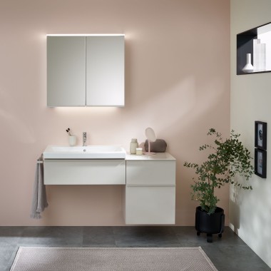 Casa de banho com móveis, lavatório e espelho Geberit em frente a uma parede de cor pastel.