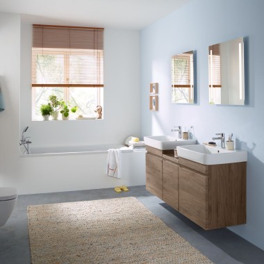 Casa de banho familiar com parede azul celeste e móveis de casa de banho em nogueira hickory, espelhos, placa de descarga e louças sanitárias Geberit