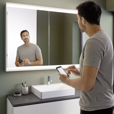 Um homem controla a iluminação do armário com espelho Geberit ONE a partir do seu smartphone (© Geberit)